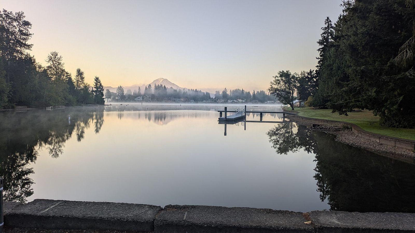 Calm Lake Tapps at sunrise with a dock in the foreground and Mount Rainier on the horizon