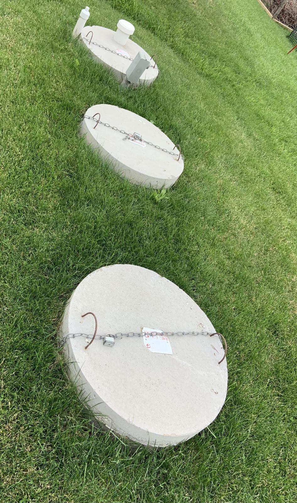 Three round concrete septic tank lids set flush in a green lawn