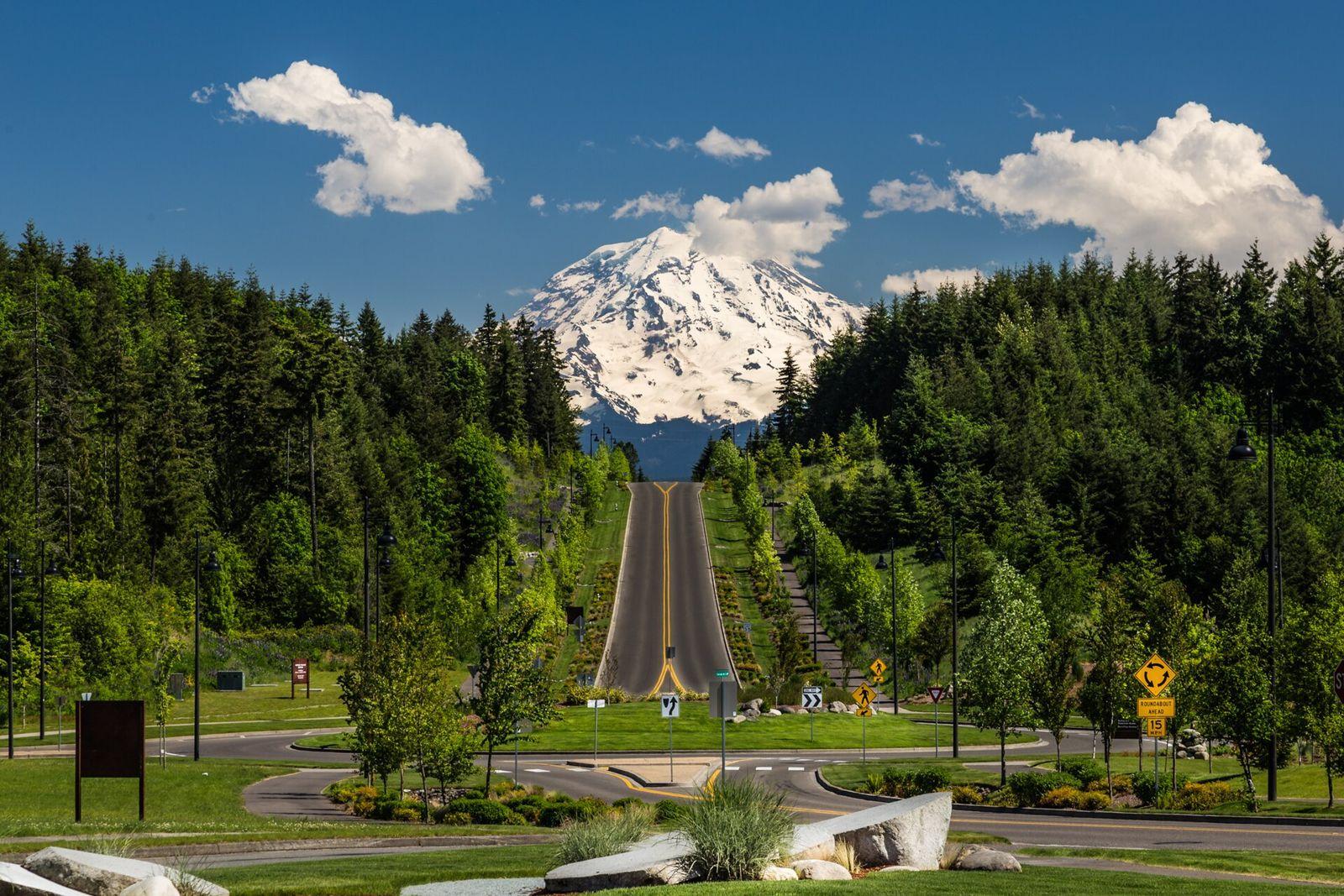 Mount Rainier rising above evergreen hills and a long straight road at The Post at Tehaleh